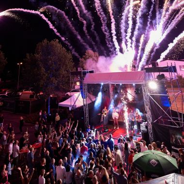 Blick auf die Bühne mit der feiernden Gesellschaft. Darüber Feuerwerk